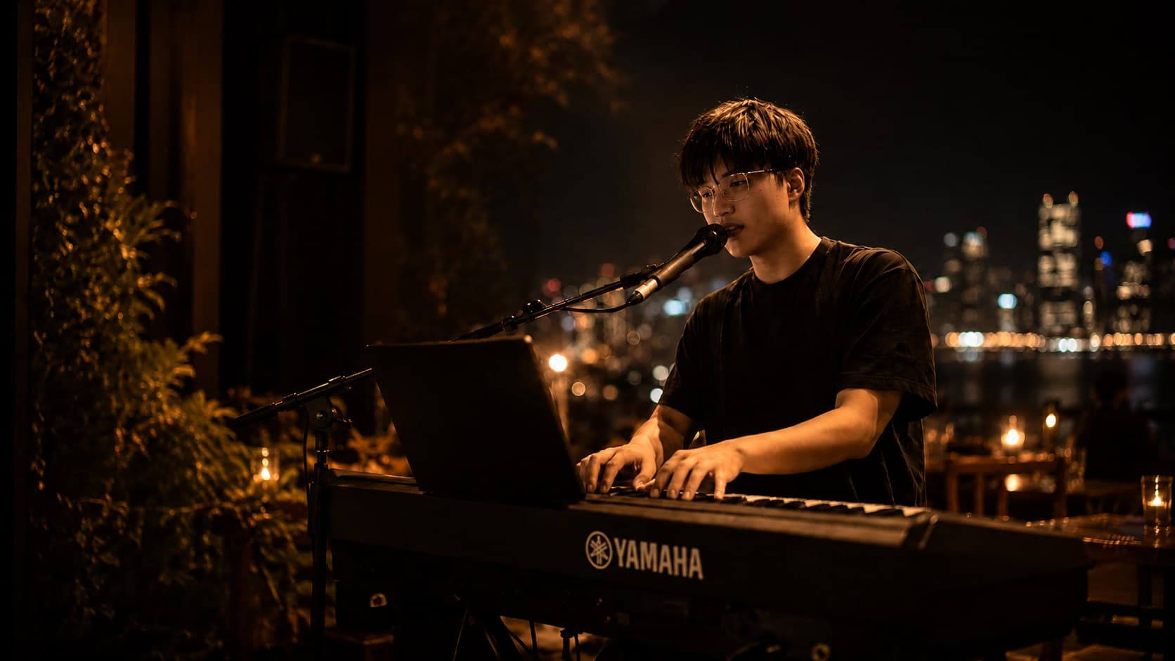 Botian Ye performing keyboard vocals beside a microphone in a warm Sydney evening venue.